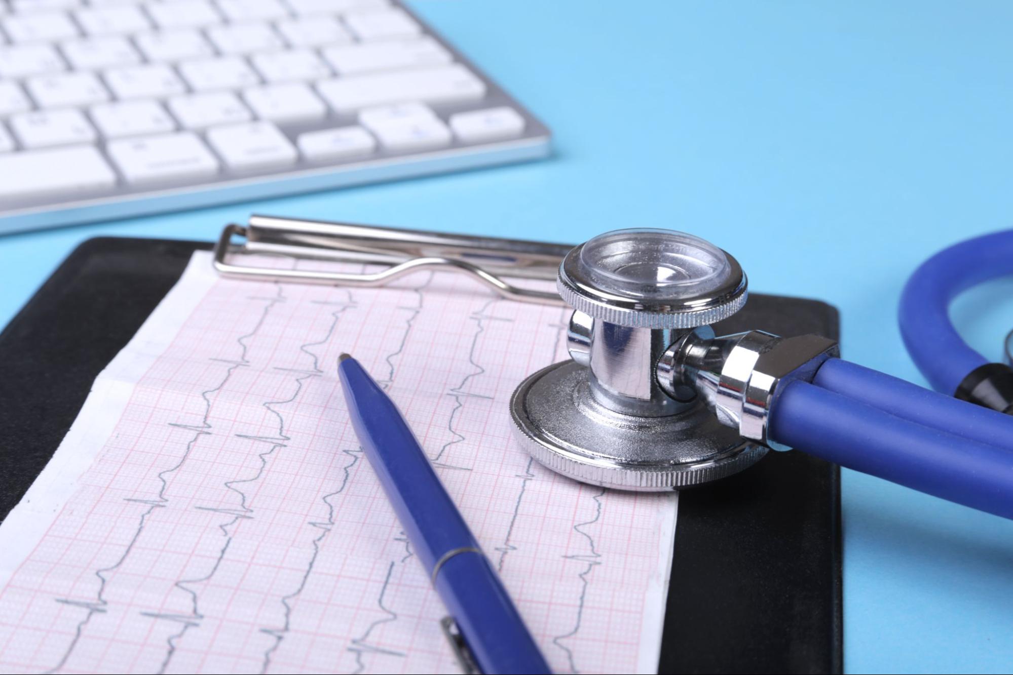 Záznam EKG srdca na papieri s modrým perom a stetoskopom na stole